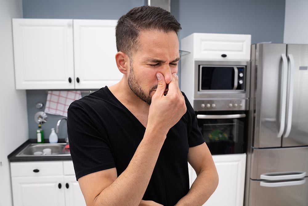 homeowner pinching nose while standing in front of kitchen sink